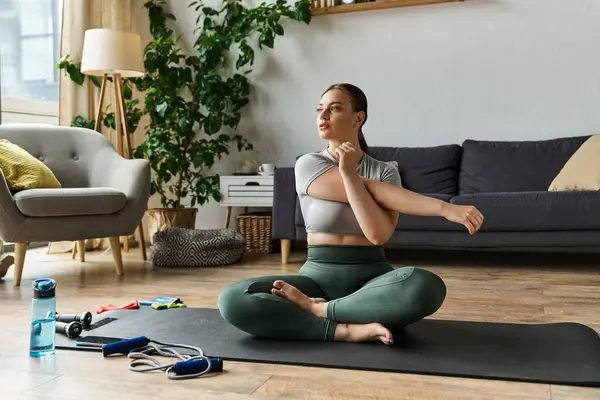 A young woman in active wear performs stretches at home, focused and preparing for her workout routine. — Stock Photo
