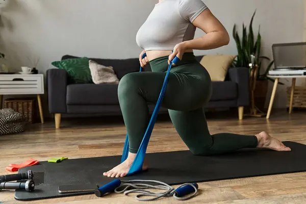 Una donna sportiva si allena a casa, concentrandosi sulla forza e la flessibilità utilizzando una fascia di resistenza. — Foto stock