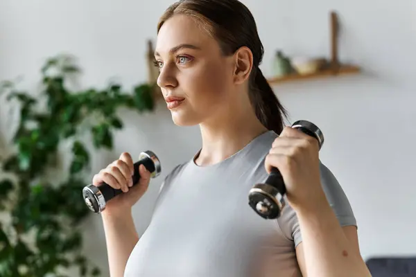 Eine junge Frau trainiert zu Hause mit Kurzhanteln und konzentriert sich dabei auf ihre Fitness und ihr Wohlbefinden. — Stockfoto