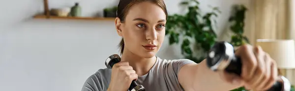 Sportive young woman in stylish active wear lifts weights while enjoying a productive home workout. — Stock Photo