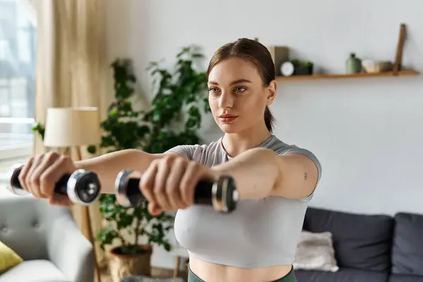 Une jeune femme se concentre sur sa routine d'exercice à la maison, tenant des poids et restant en forme dans une tenue active élégante. — Photo de stock