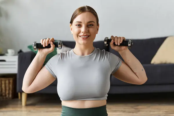 Diese junge Frau demonstriert ihre Stärke beim Training zu Hause und stemmt Gewichte in schicker Aktivkleidung. — Stockfoto