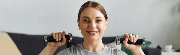 A sporty young woman engages in a home workout, lifting dumbbells while wearing stylish activewear. — Stock Photo