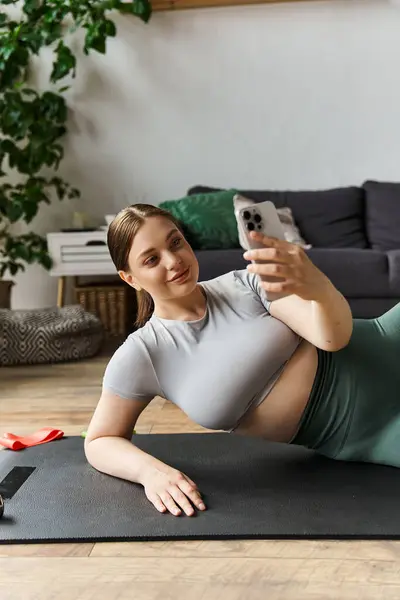 Uma jovem esportiva se exercita em casa em um top de cultura, concentrando-se em seu treino enquanto toma uma selfie. — Fotografia de Stock