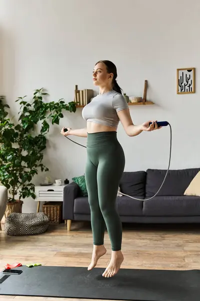 A sportive woman exercises energetically at home, skipping rope in comfortable athletic attire. — Stock Photo