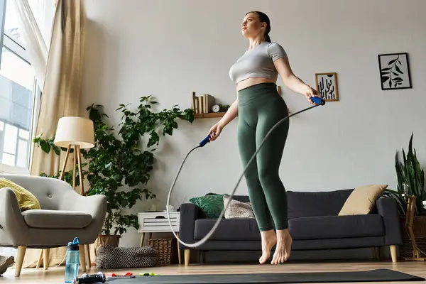 A dedicated young woman exercises at home, skipping rope in her trendy crop top and leggings. — Stock Photo