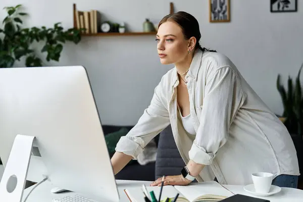 A dedicated young woman is working from home, leaning over her computer in a cozy, stylish environment. — Stock Photo