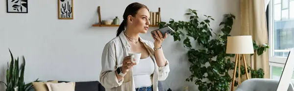 Die junge Frau hält mit einem Kaffee in der Hand inne, während sie am heimischen Arbeitsplatz telefoniert. — Stockfoto