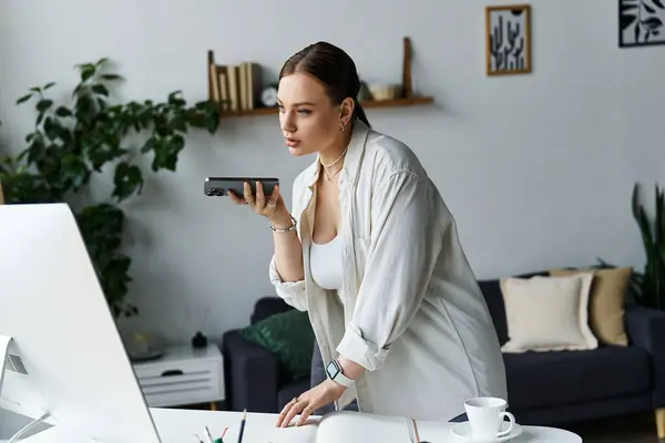 Una joven enfocada en atuendo casual se involucra en una llamada de voz en la configuración de su oficina en el hogar, mostrando productividad. - foto de stock