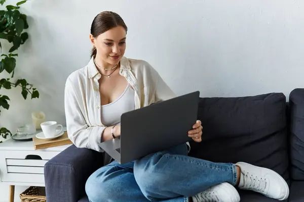 A young woman sits comfortably on her couch, focusing on work while surrounded by a serene home office environment. — Stock Photo