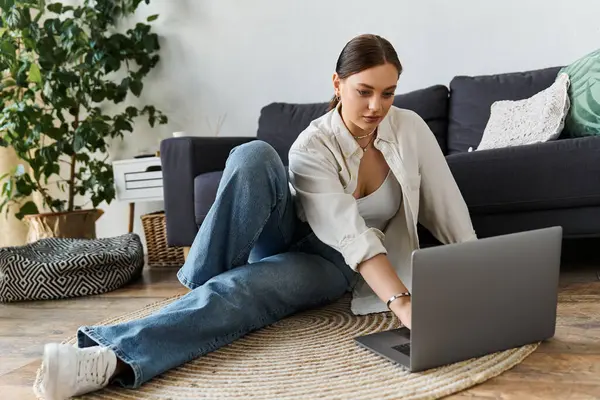 A young woman works on her laptop from a cozy living room, surrounded by plants and stylish decor. — Stock Photo