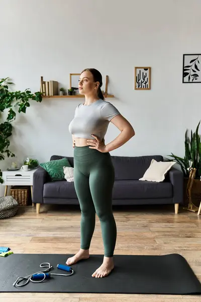 A jovem mulher esportiva confiantemente fica em seu tapete, pronta para iniciar sua sessão de treino em casa focada no exercício.. — Fotografia de Stock