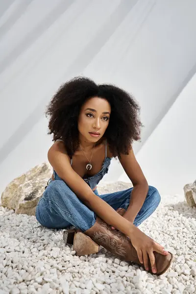A fashionable young African American woman showcases her unique style while seated on pebbles. — Stock Photo