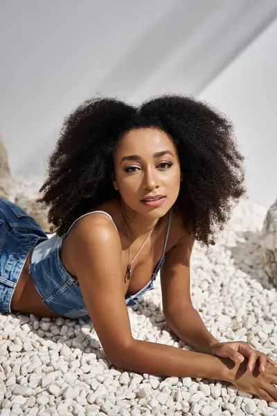 The radiant woman showcases her fashion sense while lying on a bed of white pebbles. — Stock Photo
