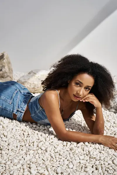 A beautiful young woman in fashionable attire lounges on a bed of smooth pebbles, exuding elegance. — Stock Photo