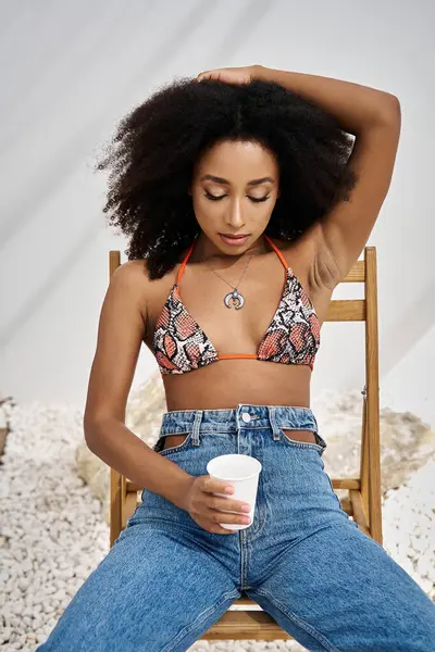 A beautiful young woman sits gracefully, embracing her style and savoring a refreshing drink. — Stock Photo