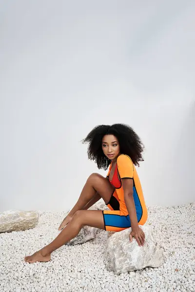 A beautiful young African American woman showcases her fashion sense while seated on smooth stones. — Stock Photo
