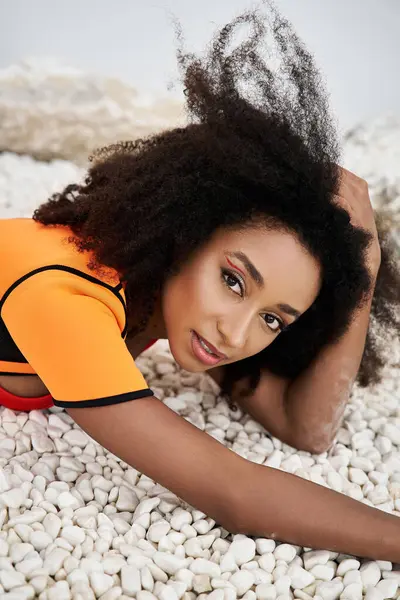 A beautiful young woman showcases her fashionable attire while relaxing on smooth pebbles. — Stock Photo