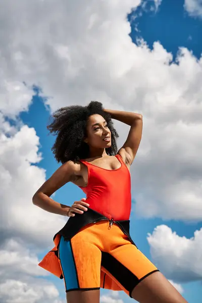 A vibrant young woman showcases her style with a striking pose under a blue and cloudy sky. — Stock Photo
