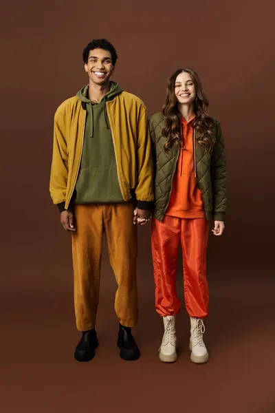 A stylish young couple stands hand in hand, showcasing their vibrant autumn fashions with joy. — Stock Photo