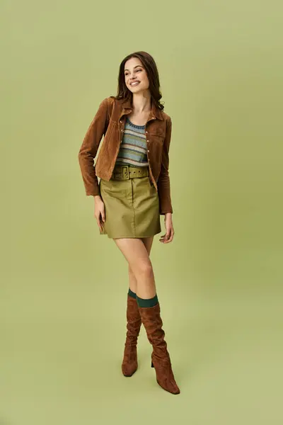 A young woman showcases her trendy autumn outfit, smiling joyfully against a green backdrop. — Stock Photo