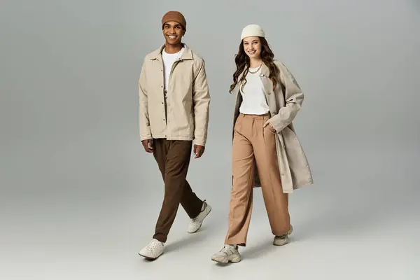 A fashionable couple strolls confidently in colorful autumn outfits amid falling leaves. — Stock Photo