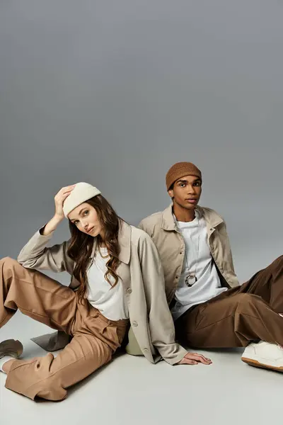 A young couple showcases trendy autumn styles while seated comfortably on a neutral surface. — Stock Photo