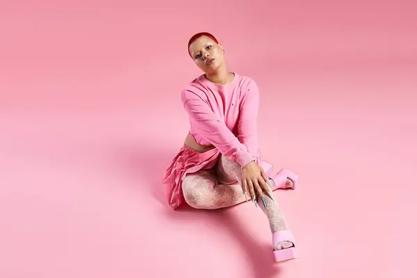 A confident young woman showcases her unique fashion with vibrant pink hair and striking accessories in a studio. — Stock Photo