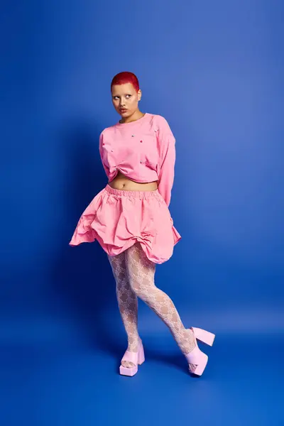 A young woman confidently displays her unique style with short pink hair and bold attire against a vivid backdrop. — Stock Photo