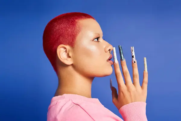 A young woman showcases her bold style with pink hair and striking nails against a blue background. — Stock Photo