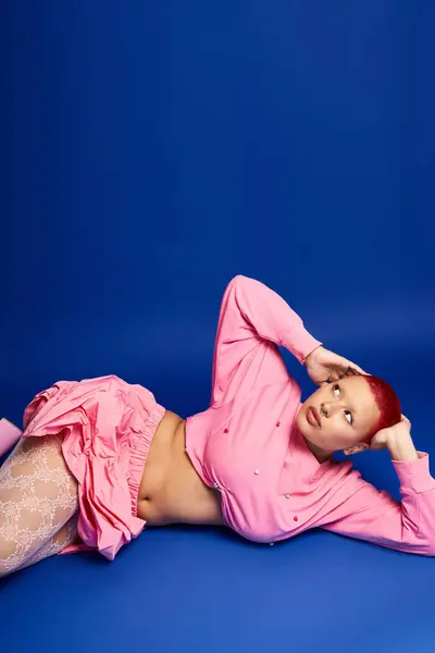 A daring young woman with pink hair and unique style poses creatively in a vibrant studio background. — Foto stock