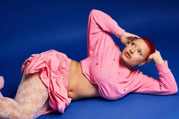 A confident young woman with vibrant pink hair showcases her bold style while posing creatively indoors. — Stock Photo