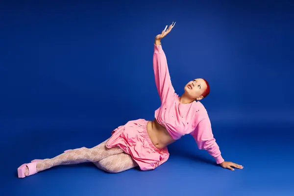 A young woman with striking pink hair and a nose piercing expresses her unique fashion sense in a studio. — Stock Photo