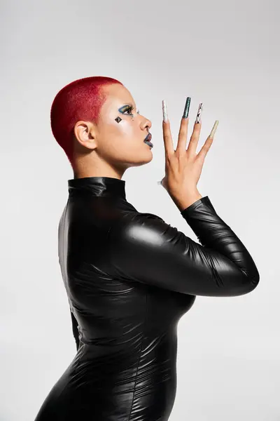 A confident young woman flaunts her unique style with pink hair and dramatic nails in a studio setting. — Stock Photo