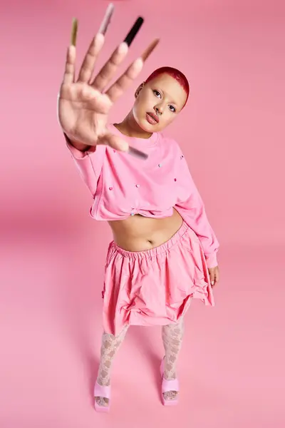 This striking young woman showcases her unique style with short pink hair and bold accessories in a lively studio. — Stock Photo