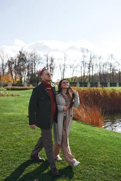 A couple enjoys a romantic walk by the water, dressed warmly for a beautiful autumn day. — Stock Photo