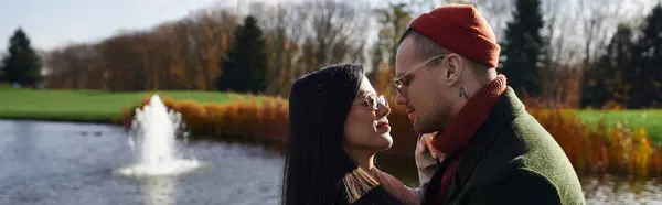 A warm moment shared between a couple dressed in autumn attire beside a peaceful pond. — Stock Photo