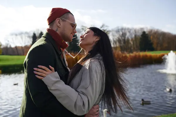 A couple embraces by a serene pond, wrapped in cozy autumn attire, enjoying each others warmth. — Stock Photo