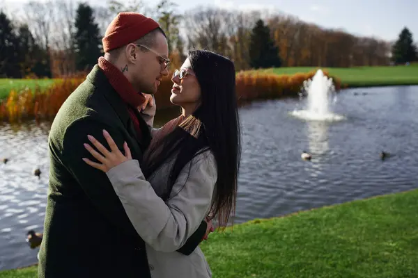 A couple shares warmth and affection by a serene pond amid autumn foliage. — Stockfoto