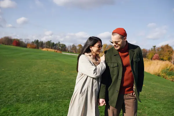 A loving couple walks hand in hand, wrapped in warm autumn attire, sharing smiles and laughter. — Stock Photo