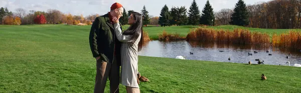 A couple enjoys a tender moment by a serene pond, surrounded by vibrant autumn foliage. — Stock Photo