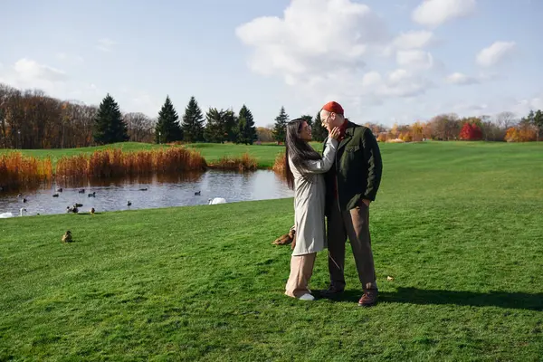 A loving couple shares a warm moment together by a peaceful pond on a bright autumn day. — Stock Photo
