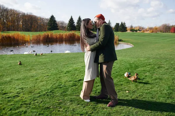 A loving couple enjoys a warm moment together while surrounded by autumn colors near a serene pond. — Stock Photo