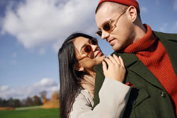 Un couple joyeux dans une tenue d'automne confortable embrasse dans un cadre extérieur dynamique, entouré par la nature. — Photo de stock