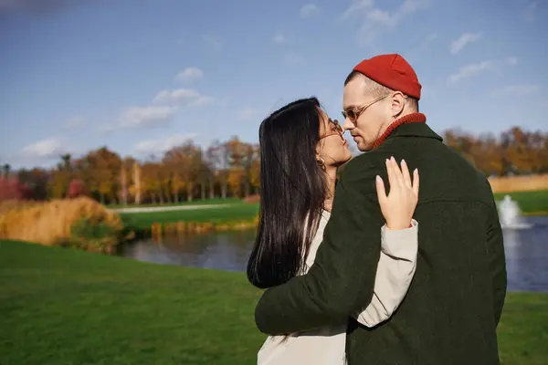 A loving couple enjoys a warm embrace, surrounded by vibrant autumn foliage near a tranquil lake. — Stock Photo