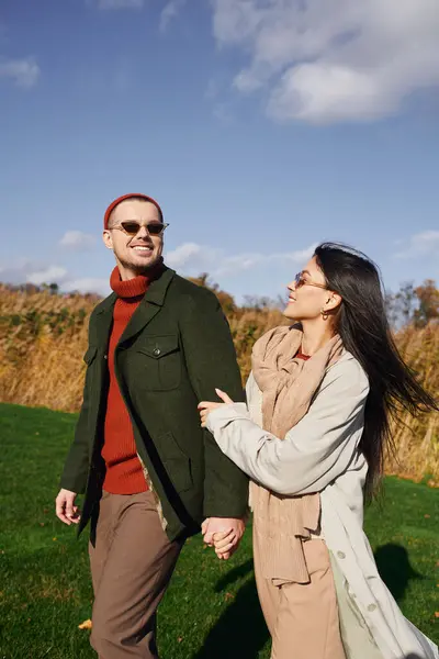 A couple enjoys a playful walk in cozy attire amidst golden autumn foliage and a clear sky. — Stock Photo