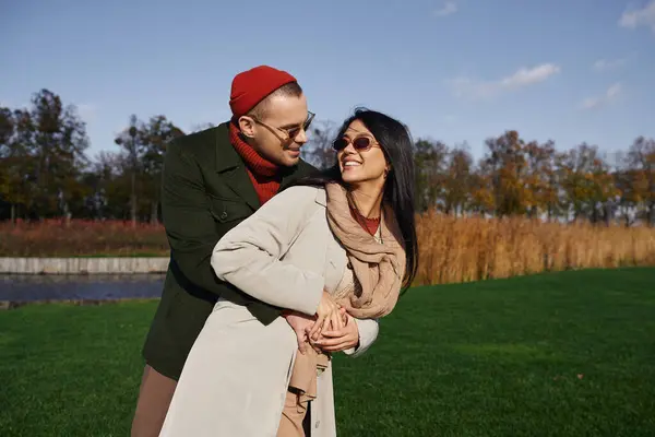 A happy couple embraces outdoors, sharing warmth in autumn layers against a vibrant background. — Foto stock