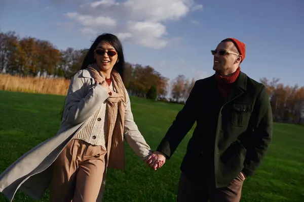 A couple walks hand in hand, dressed warmly for an autumn day, surrounded by colorful trees. — Stock Photo