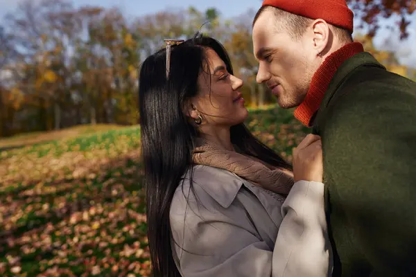 A couple shares a tender moment, wrapped in warm autumn attire, surrounded by colorful leaves. — Stock Photo
