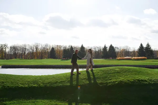 A couple enjoys a romantic walk hand in hand on a crisp autumn day by the tranquil lake. — Foto stock